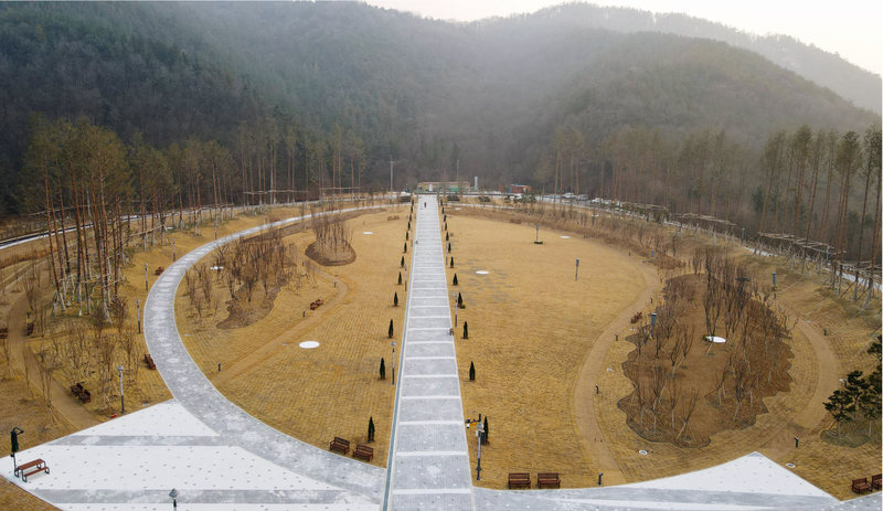 하늘에서 본 개장 전 다온숲 — 갈색 겨울 잔디밭을 둘러싼 원형 산책로와 가운데 곧은 길, 뒤쪽의 산